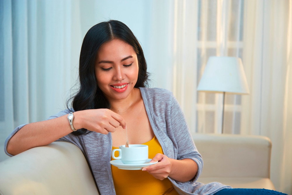 Smiling woman dunking a tea bag in a cup.