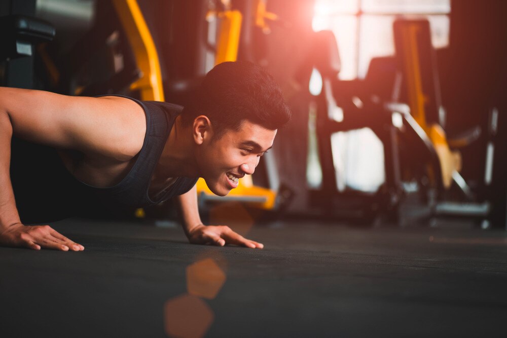 Young Asian male flashes a smile while doing push-ups at a gym.