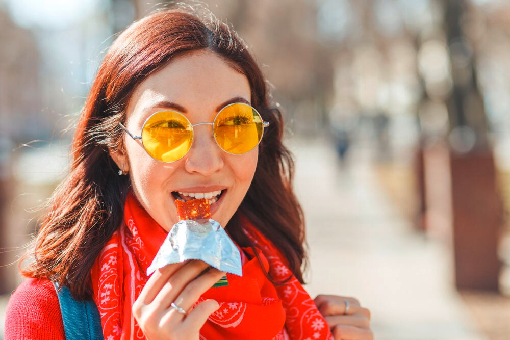 Woman with yellow-tinted sunglasses eating a cereal bar.