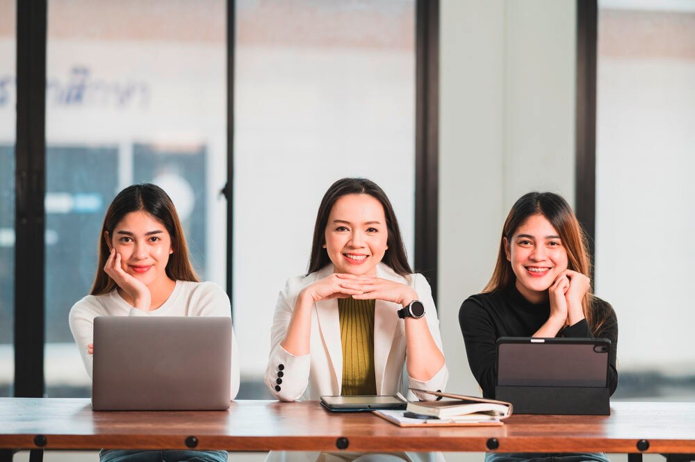 Three Asian females of various ages pose inside a university classroom.