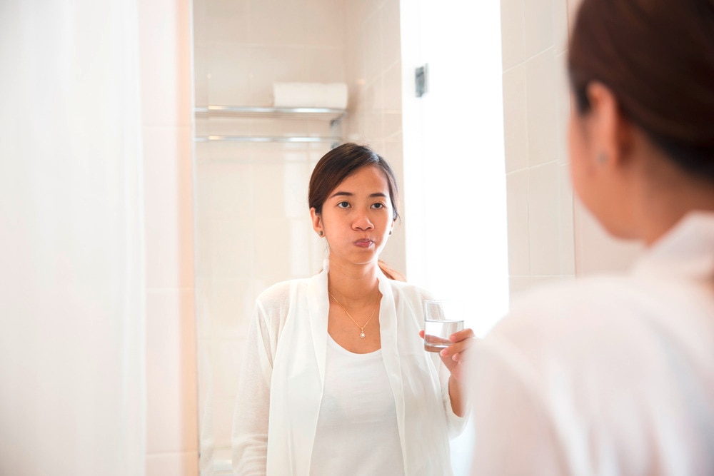 Young Asian female looks at the mirror while rinsing with mouthwash.