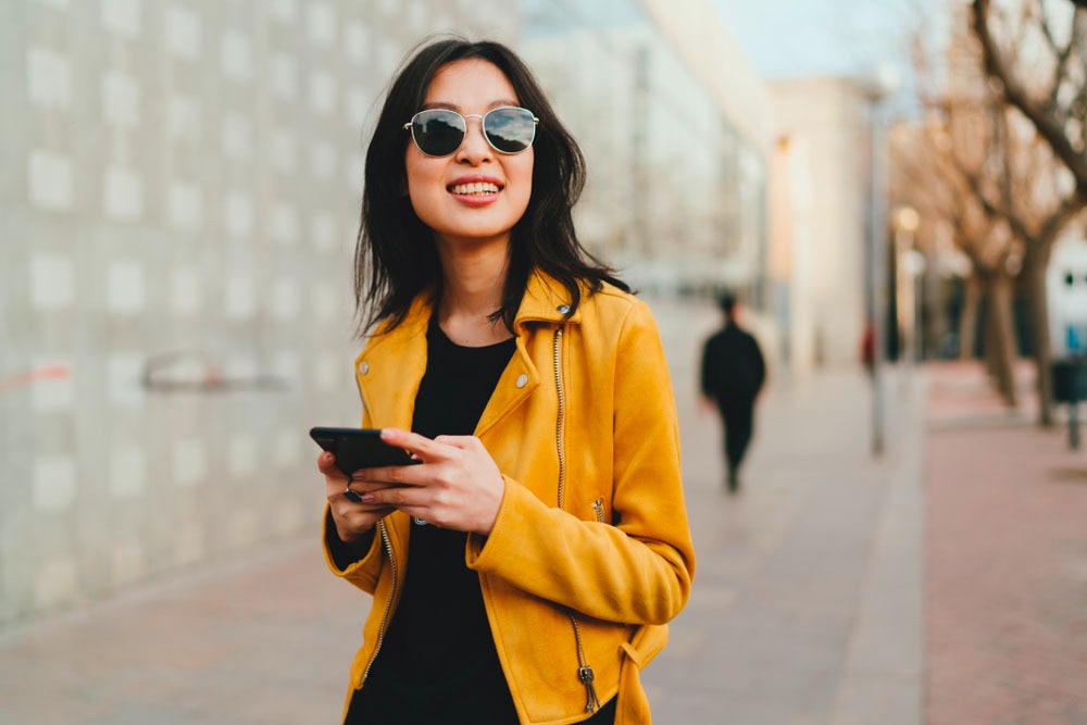 Woman in yellow leather jacket and sunglasses playing with her phone.