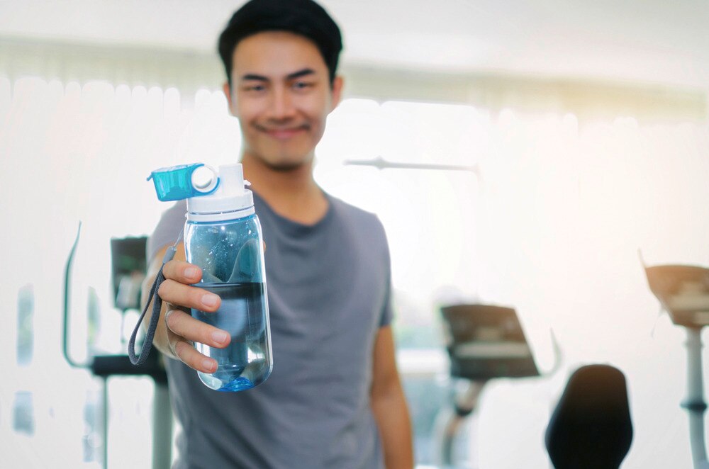 Asian man holding a bottle of water at the gym