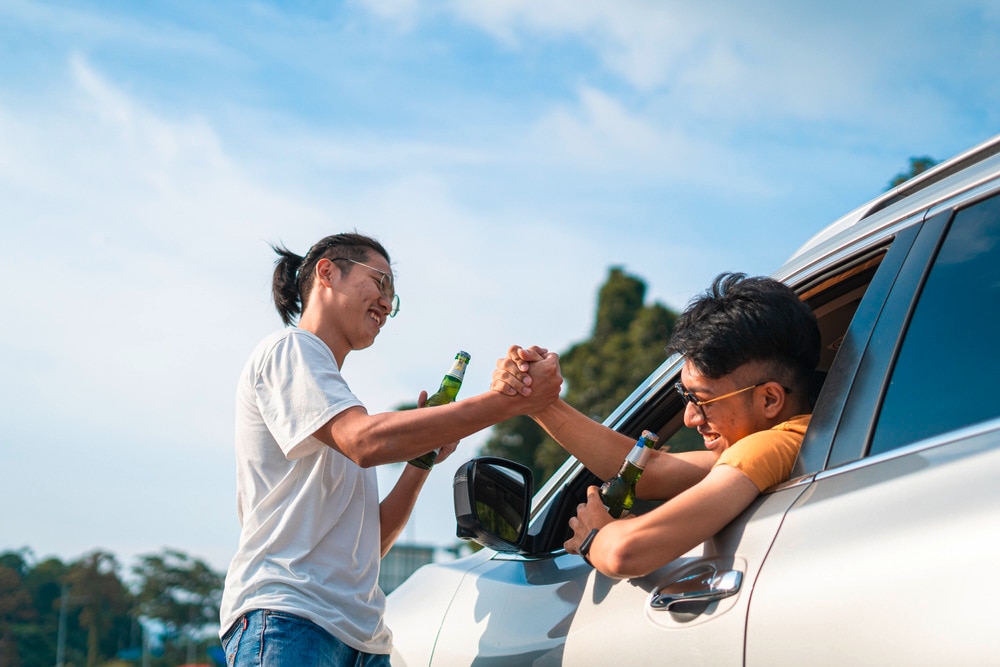 Man doing the diagonal handshake with a man inside the car.