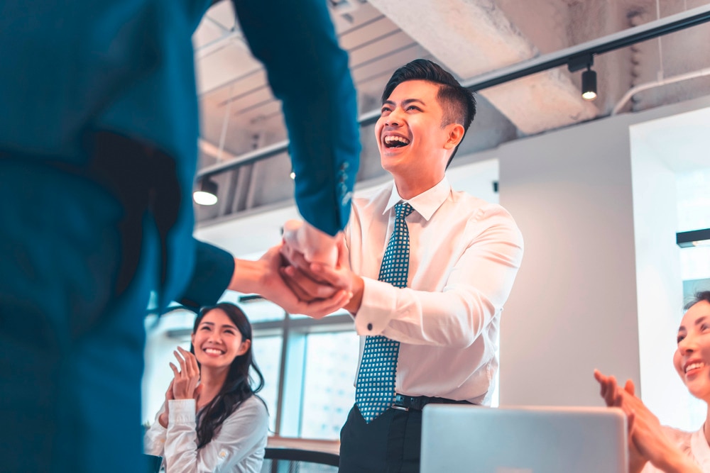 A smiling man shaking hands with unseen man at the office.