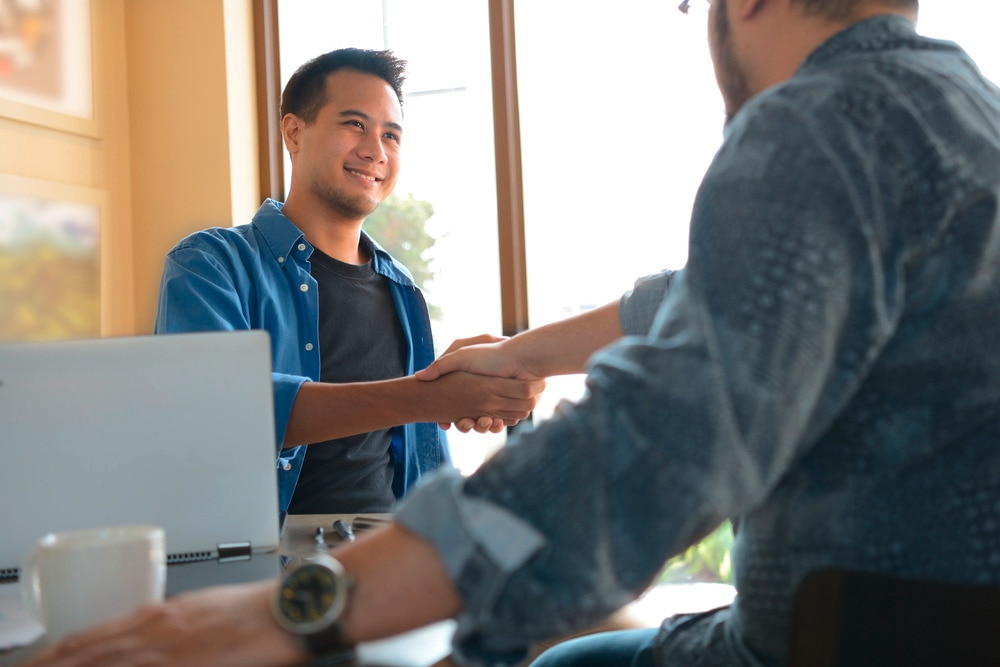 Man shaking hands with another man from across the table.