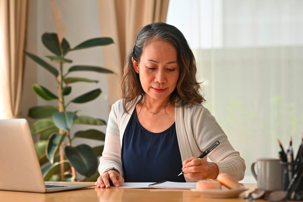 Senior woman in beige cardigan working at her home office.