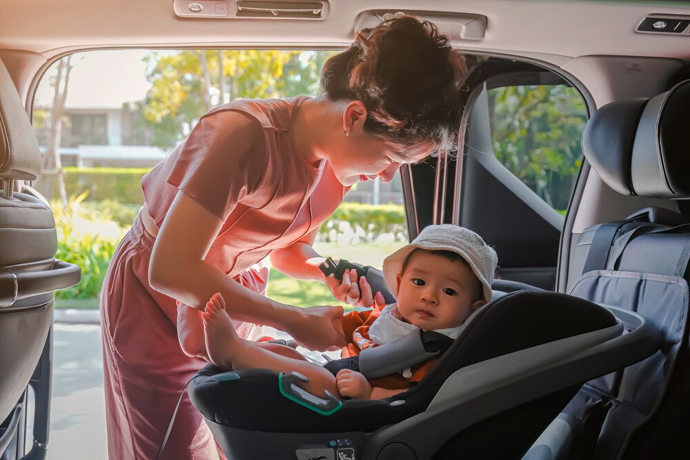 Asian mother tucking in baby in carseat.