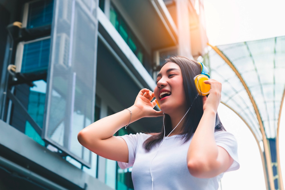 Smiling woman listening happily to music with yellow headphones.