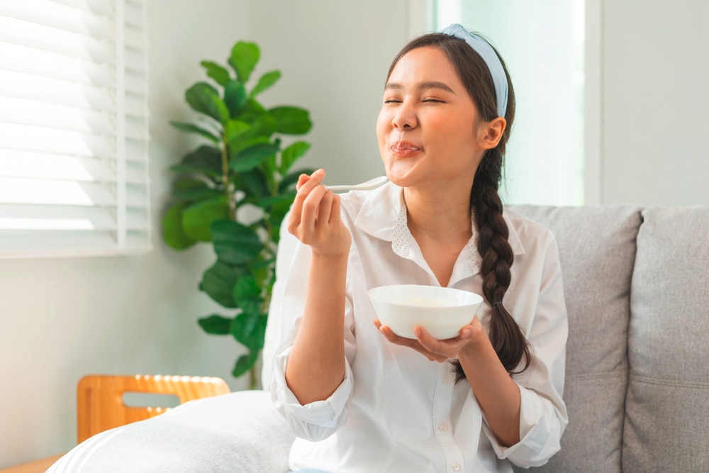 Woman eating a bowl of yogurt while sitting on a sofa.