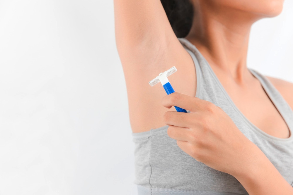 Woman shaving her underarms with blue razor.