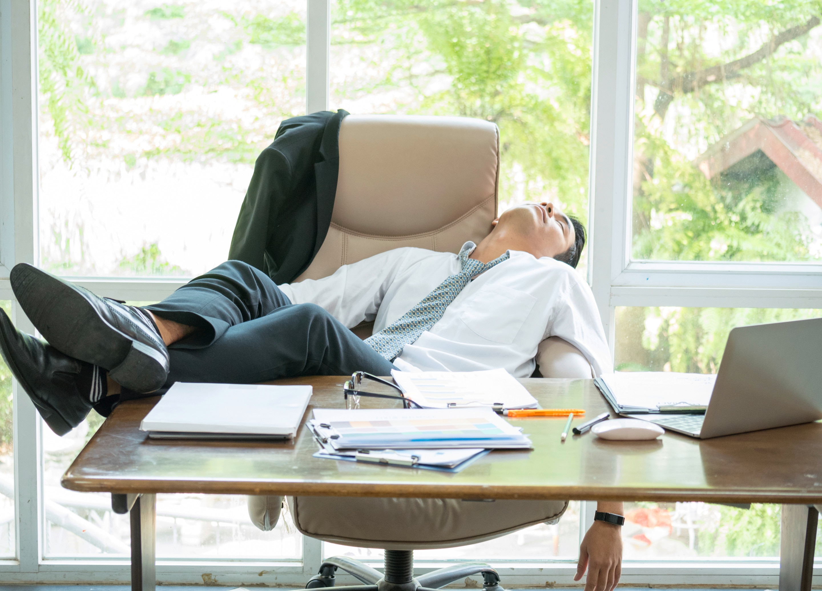 A tired Asian man sleeping at his desk with his feet on the table