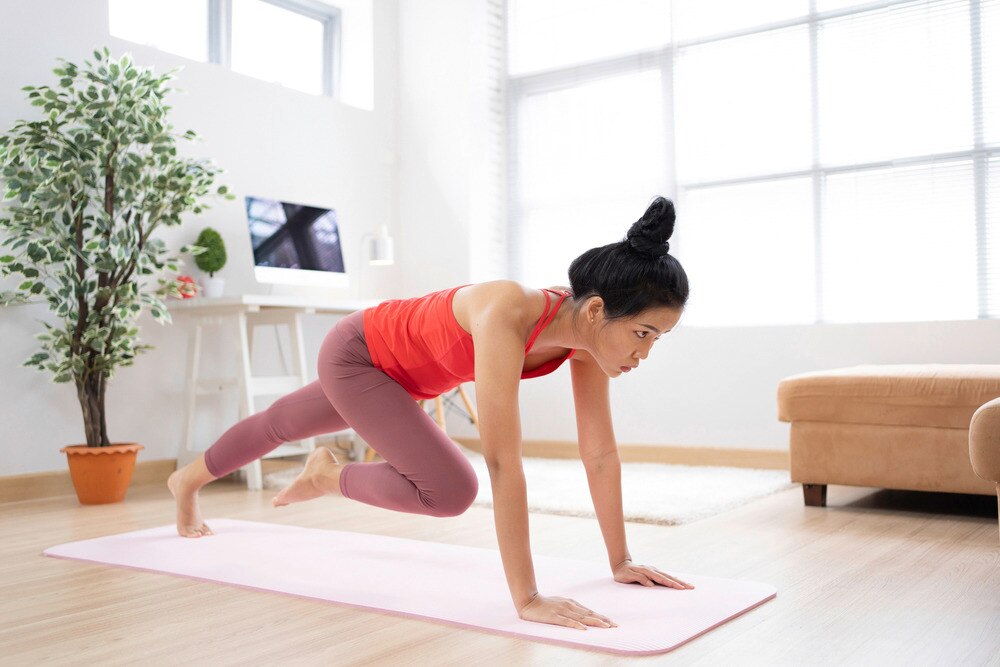 Asian woman in a bright red tank top doing mountain climbers at home