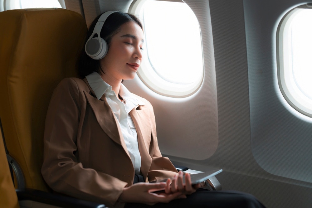 Asian woman wearing headphones while sleeping in an airplane.