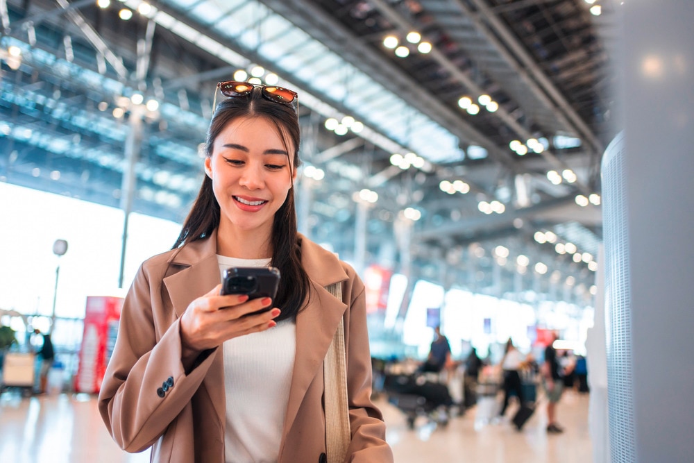 Asian woman in a brown coat texting at the airport.