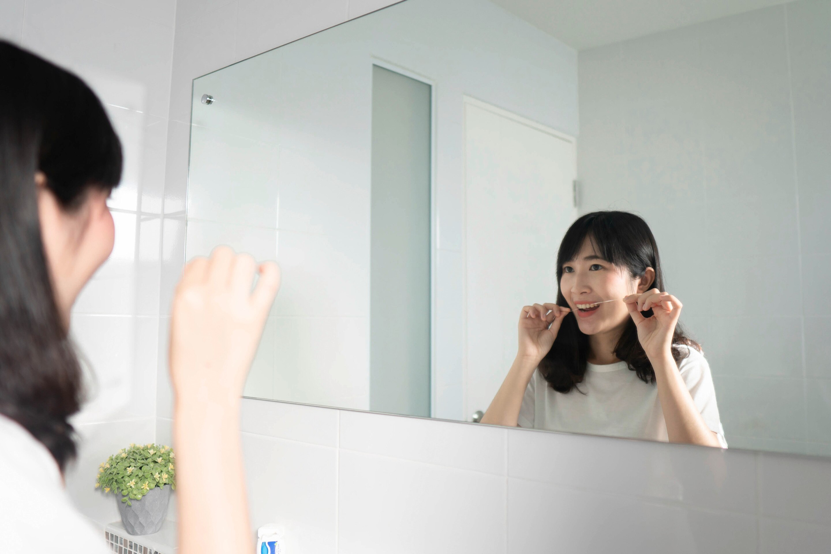 Asian woman flossing in front of a mirror.