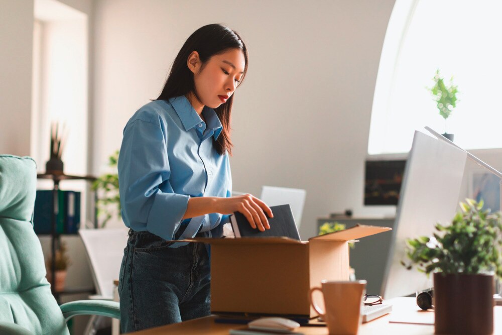 A woman in blue shirt packing her belongings at the office in a box.