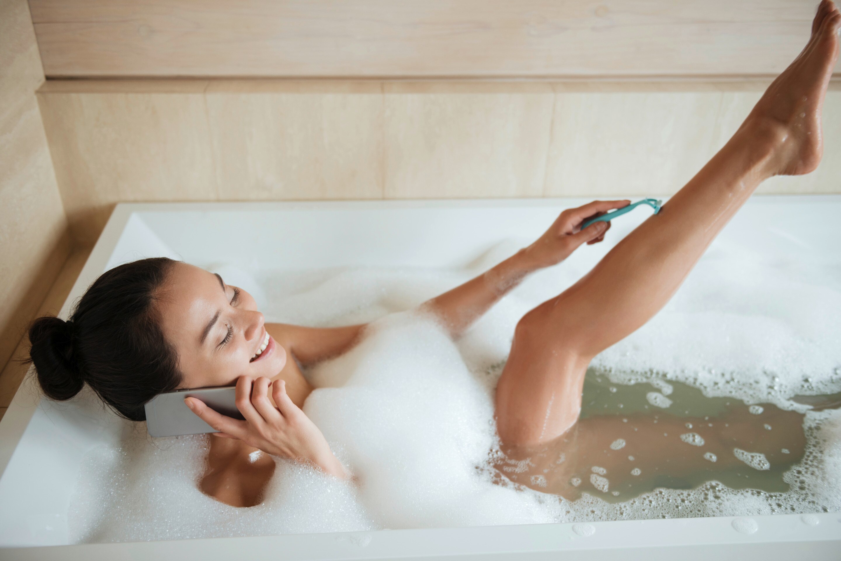 Asian woman shaving legs in a bathtub