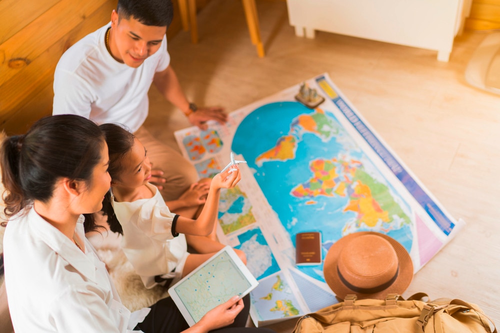 Asian family looking at a world map, with daughter playing with a toy airplane.