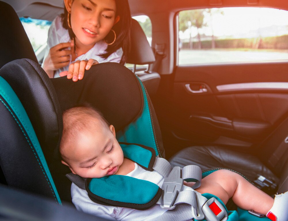Asian mom checking on sleeping baby in car seat.