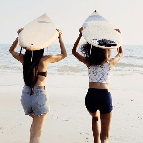 girls running towards beach with surfboard