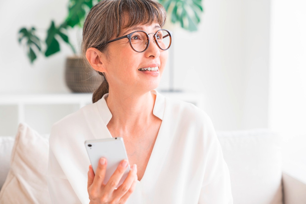 Woman with gray hair and glasses holding a white smartphone.