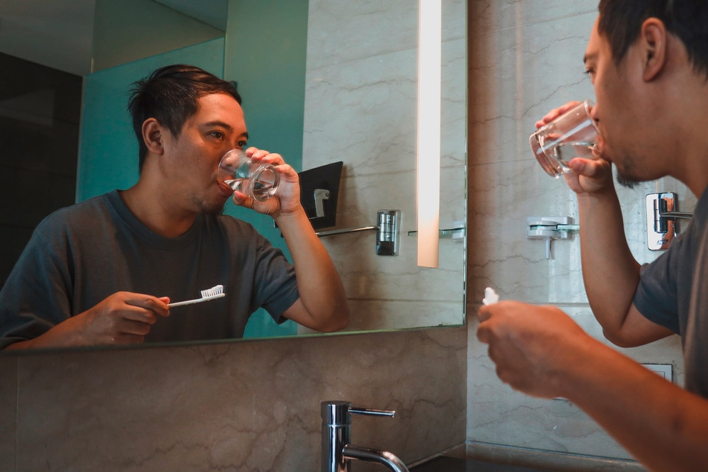 Man gargling water after brushing his teeth in the sink.