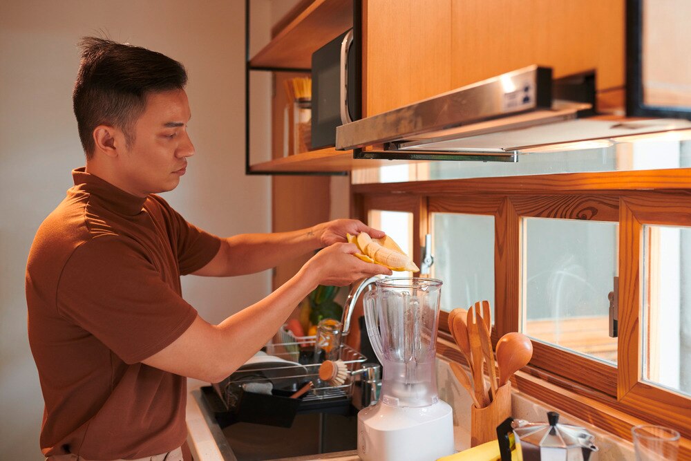 Man putting banana slices in a blender to make smoothie.