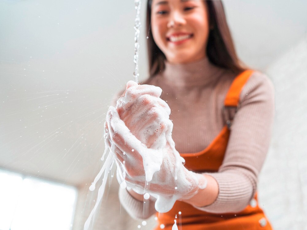 Happy woman washing her hands in the kitchen with soap.