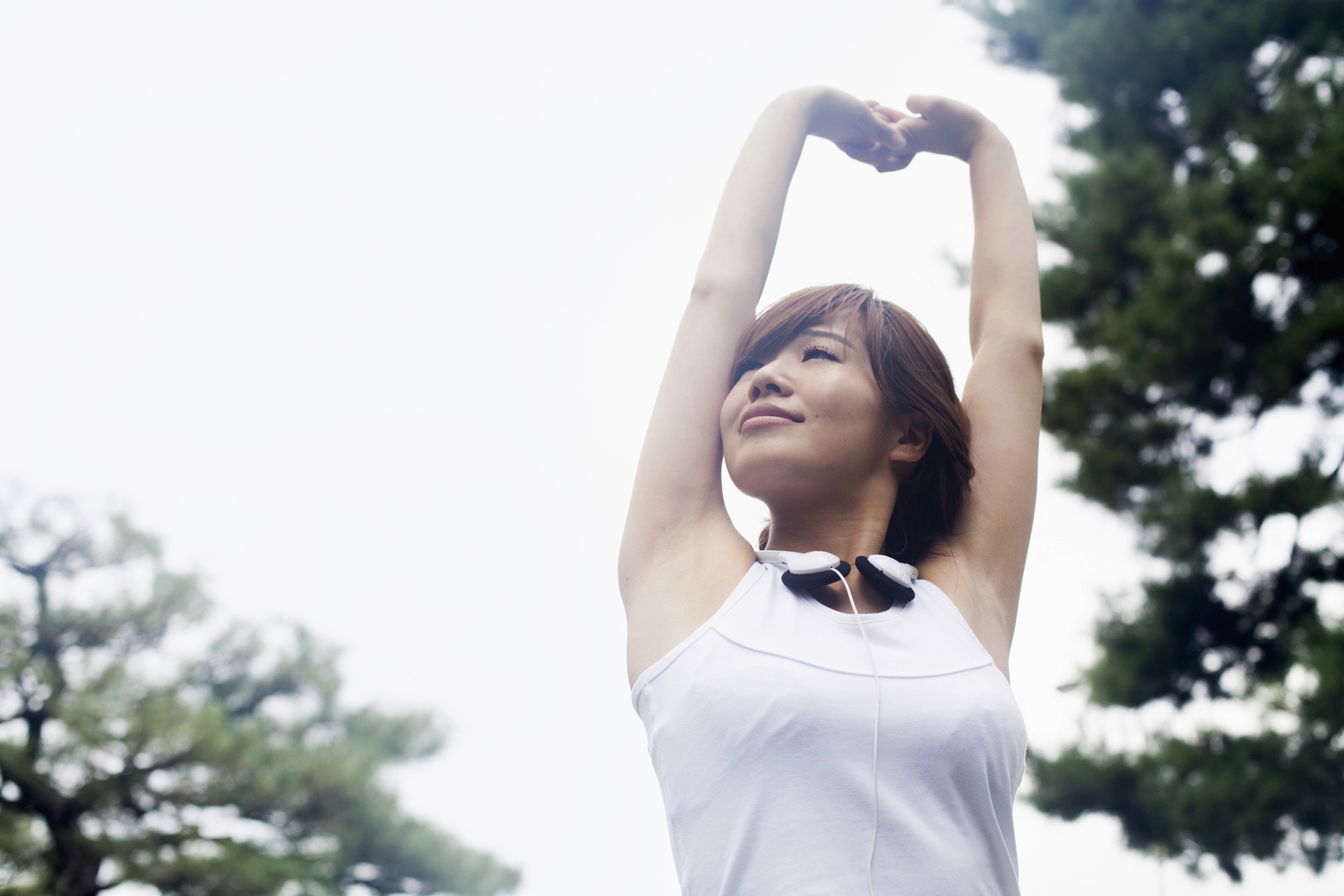 An Asian woman wearing headphones on her neck and stretching arms upwards  