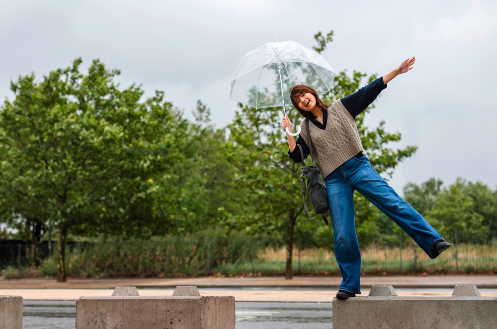 Woman holding an umbrella while jumping and dancing in the rain.