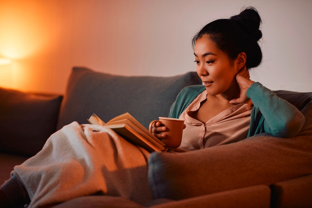 Woman holding a cup of hot cocoa while reading book.
