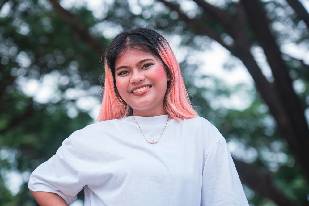A portrait of smiling woman with light pink hair.