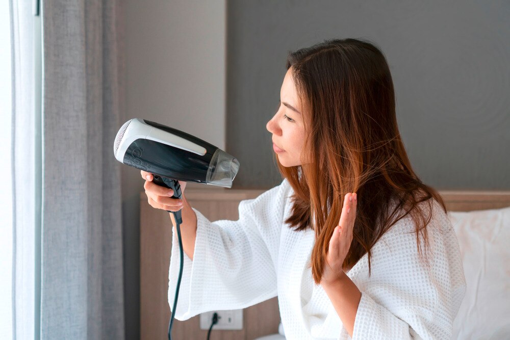A woman in her bathrobe blow drying her hair.