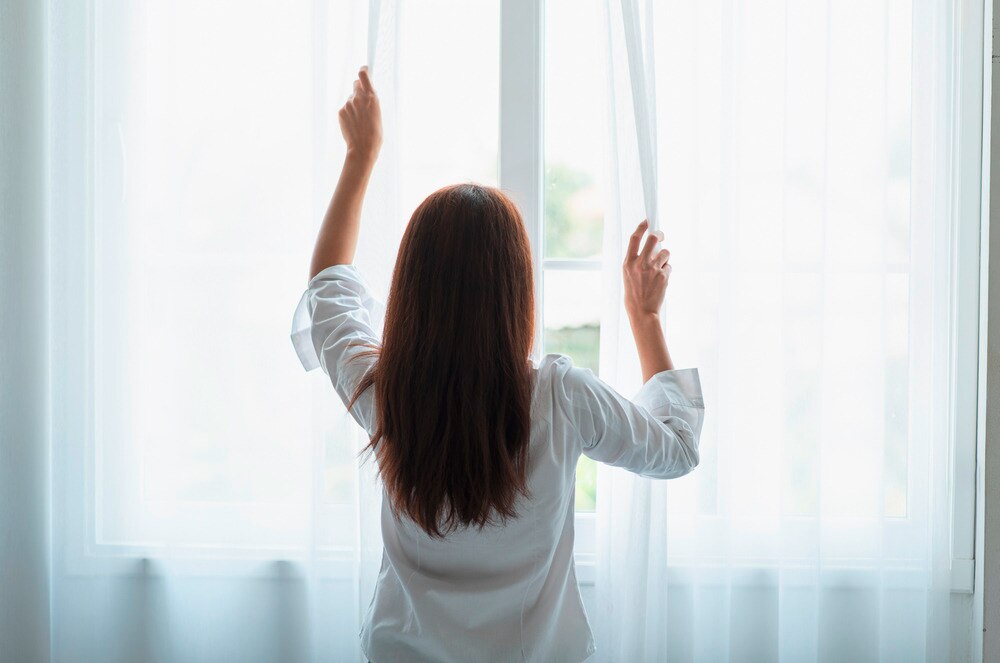 An Asian woman drawing her window curtains.