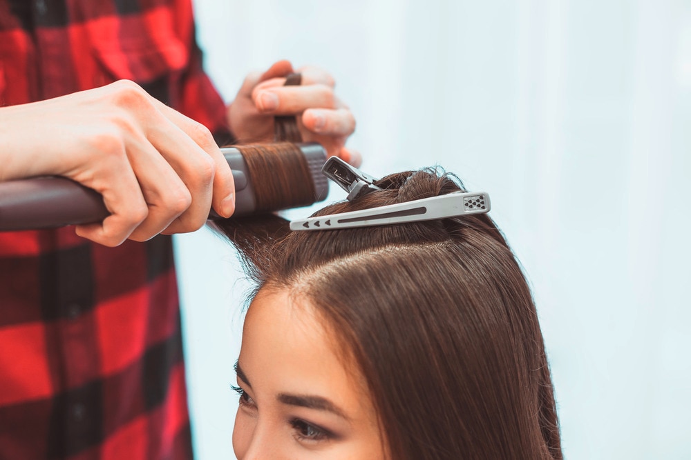 Hair stylist curling a woman’s hair with a flat iron.