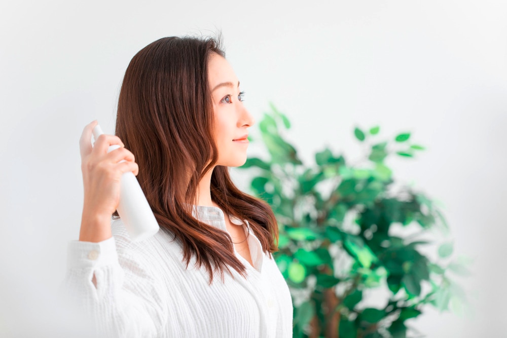 Woman spritzing hairspray to secure her loose curls.