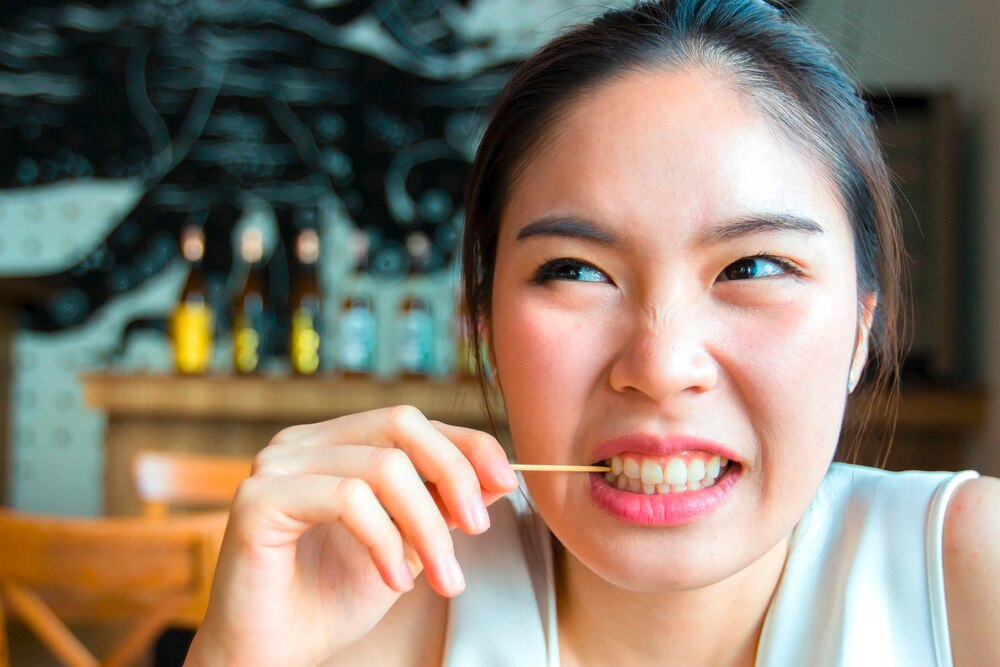 Woman using toothpick to remove stuck food between her teeth.