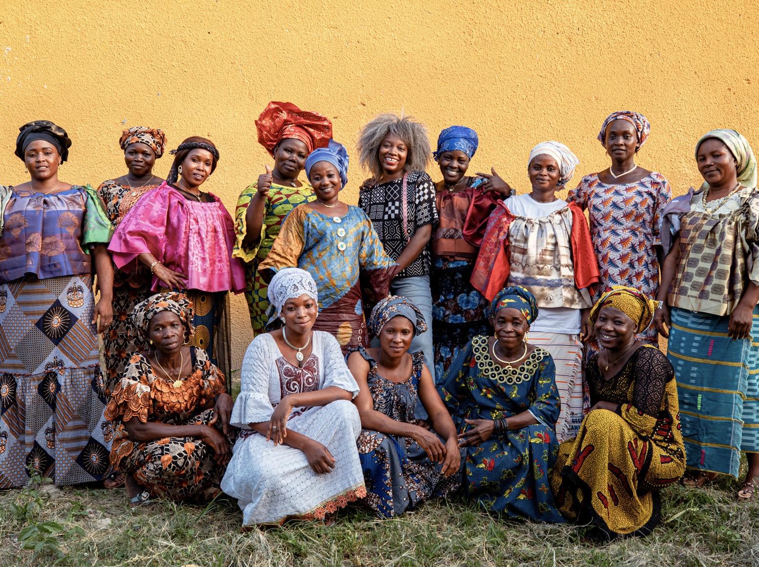 Groupe de femmes africaines souriant avec la créatrice de mode Rebecca Zoro devant un mur orange