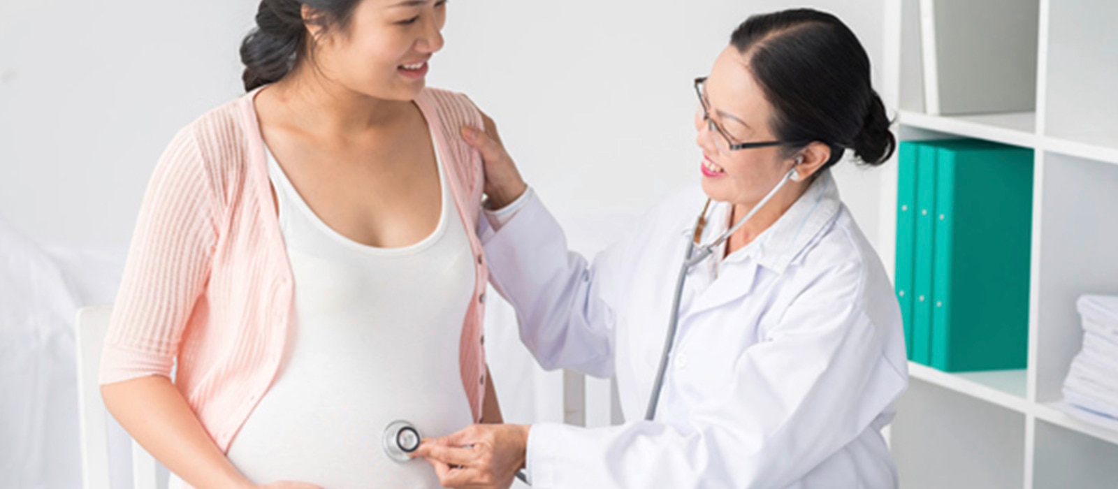 Seorang dokter sedang memeriksa perut seorang wanita hamil dengan stetoskop