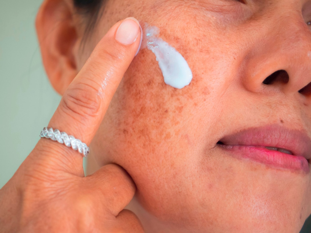 Asian woman applying cream on face.