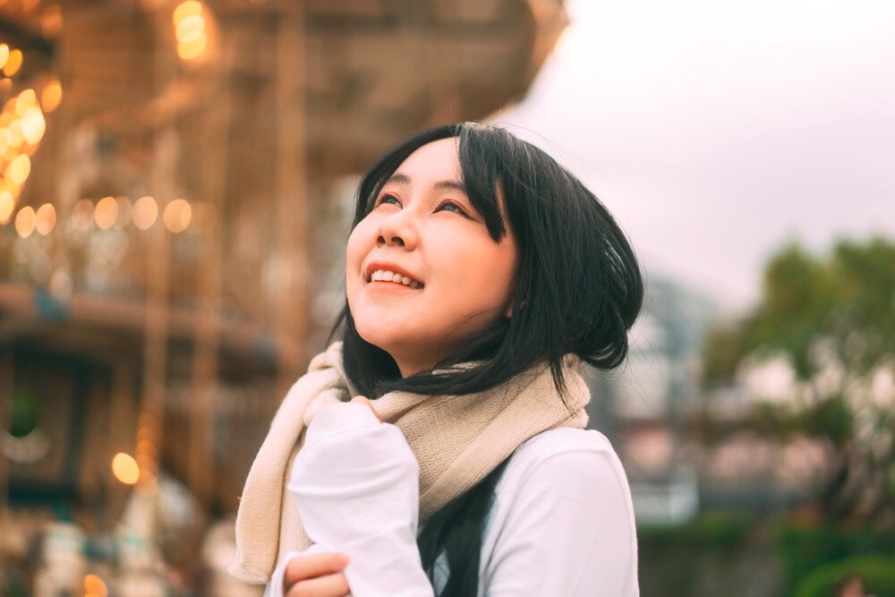 Asian woman wearing a scarf looking up at the sky.