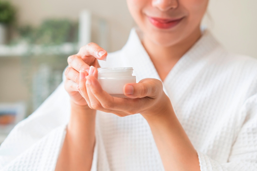 Closeup of a woman’s hand holding a jar of moisturizer.