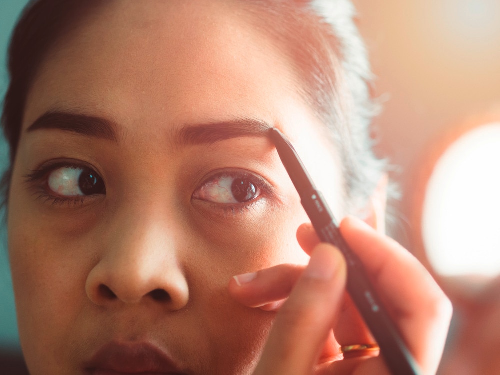 Asian woman drawing on her eyebrows.