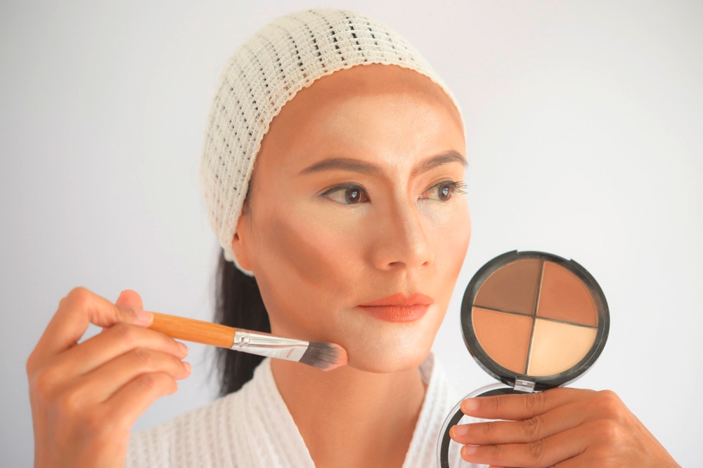 Asian woman contouring her face with makeup.