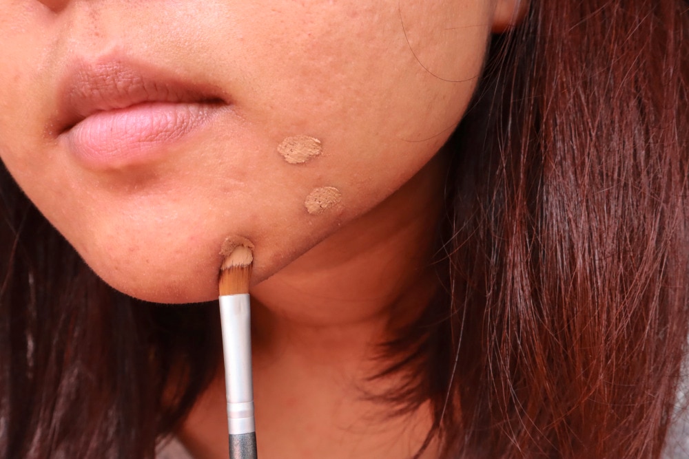 Closeup of a woman applying concealer to your blemishes.
