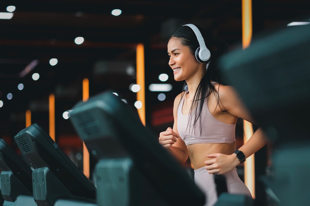 Woman wearing white headphone running on a treadmill.