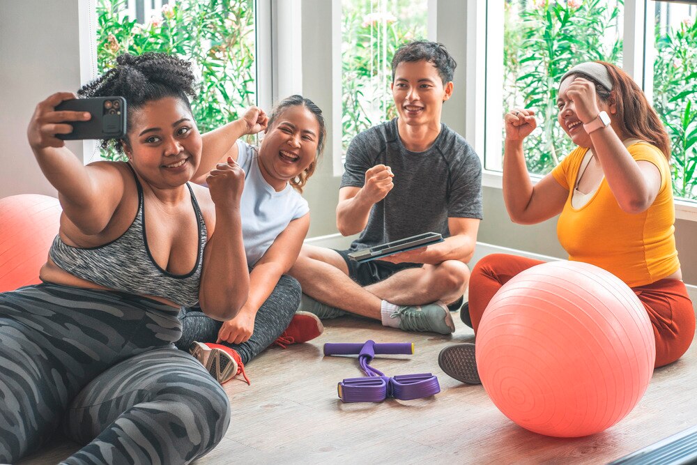 Three women and a man taking a group selfies at the gym.