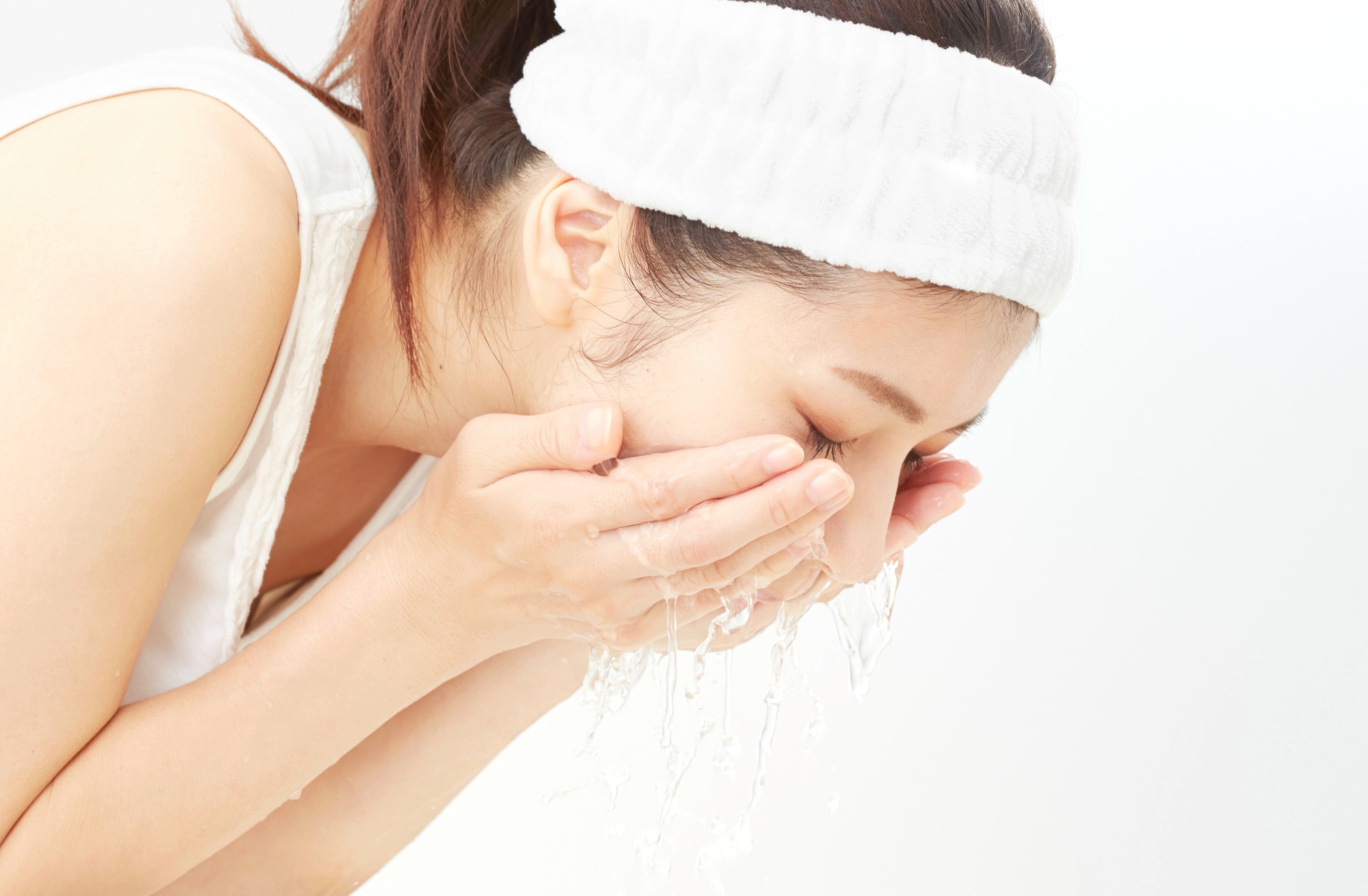 Asian woman wearing a headband while washing her face