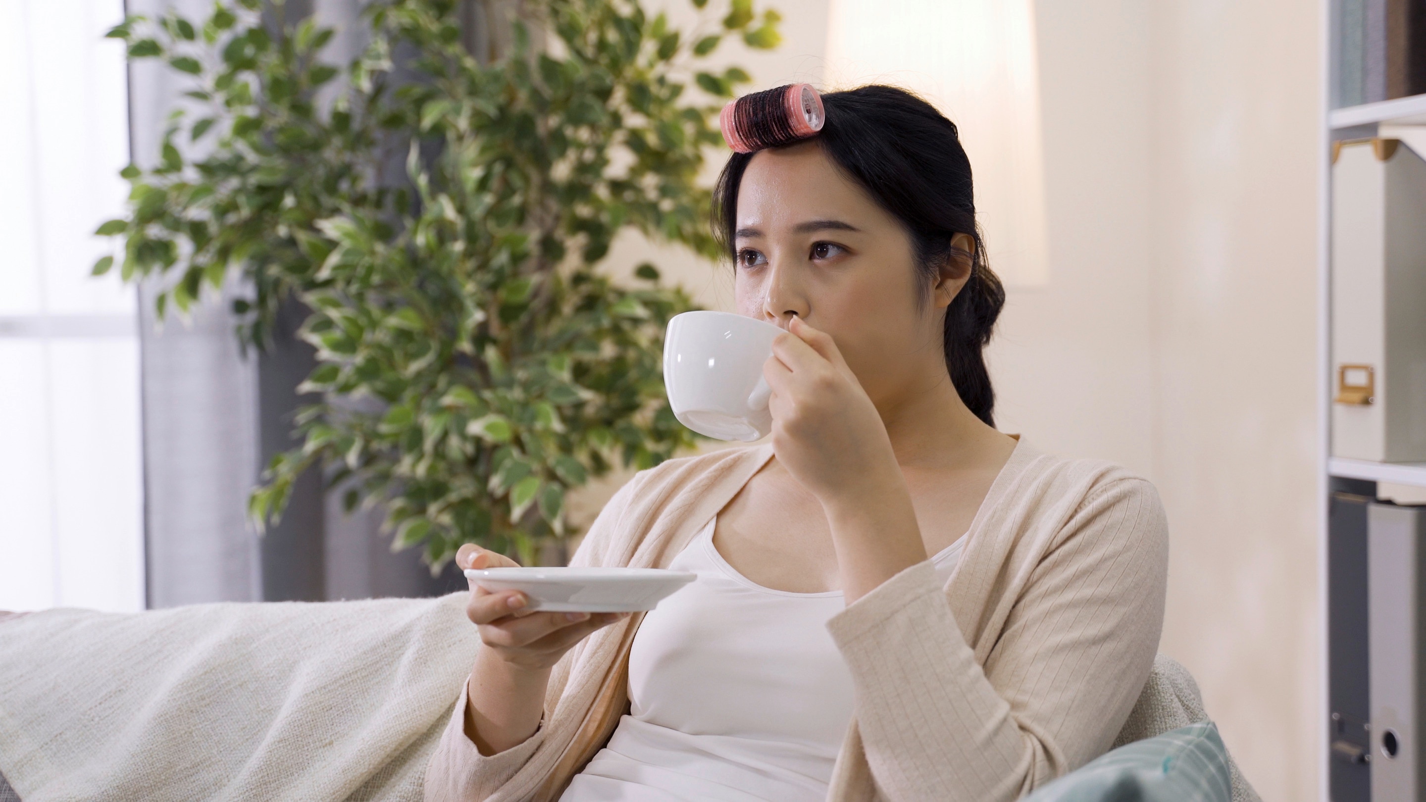 Asian woman drinking coffee wearing a hair roller.